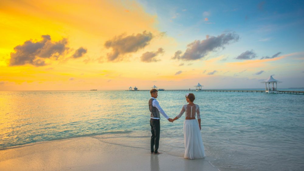 A romantic couple holding hands at sunset on a Maldives beach, exuding love and tranquility.