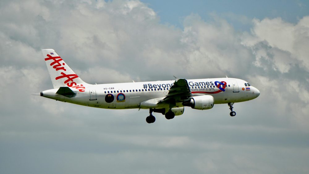 AirAsia Airbus A320 flying in clear sky with clouds, showcasing airline travel.